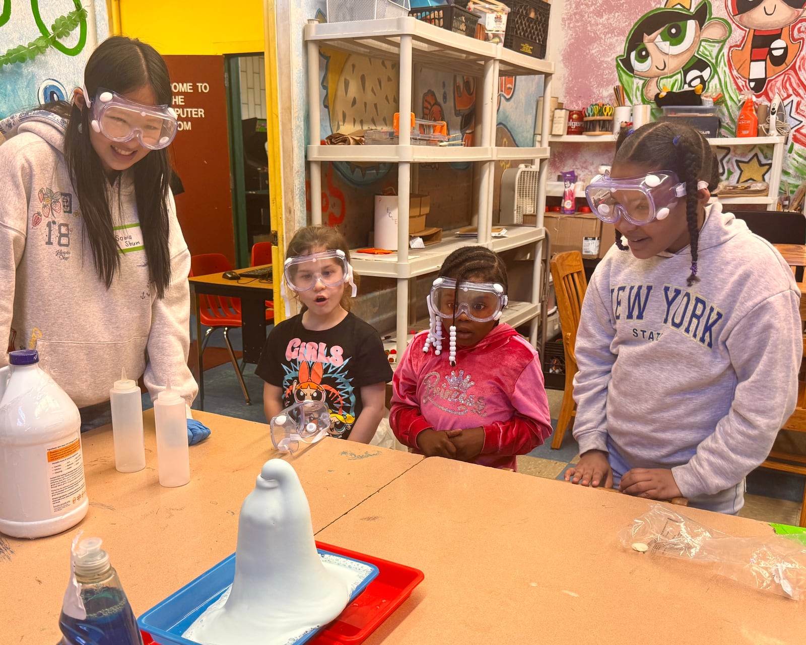 Sonia Shum and students in safety goggles watch a foaming science experiment.